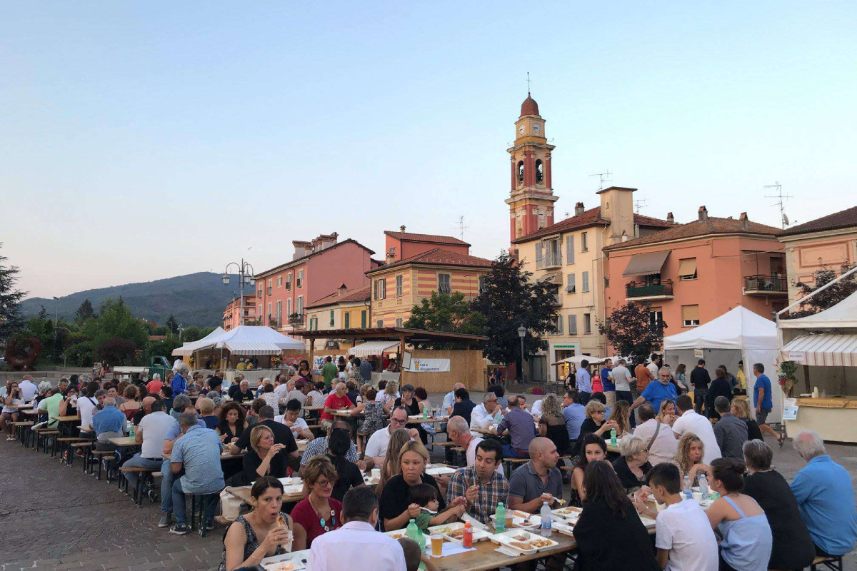 Sagra gastronomica in un borgo ligure con tavolate all’aperto e stand di prodotti tipici